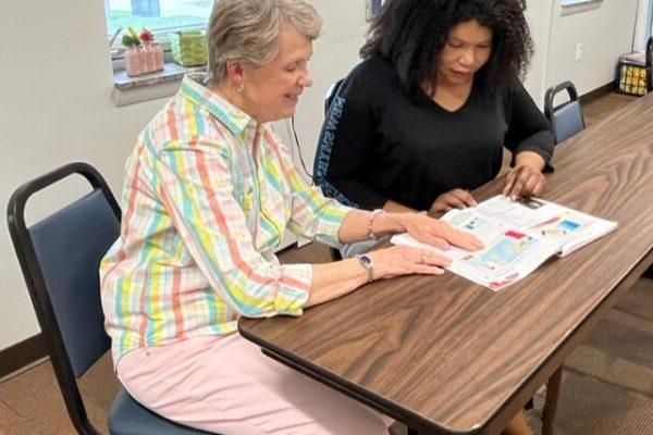 a person sitting at a table with a person looking at a piece of paper